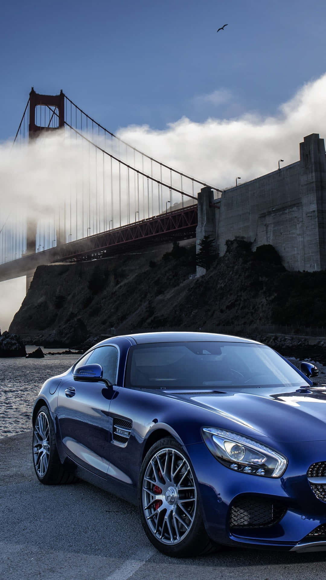 藍色AMG GT-R高架橋雲景壁紙 壁紙 — 一架時尚的藍色跑車停泊在標誌性的金門大橋附近，天空多雲，一隻海鷗在頭頂飛翔。