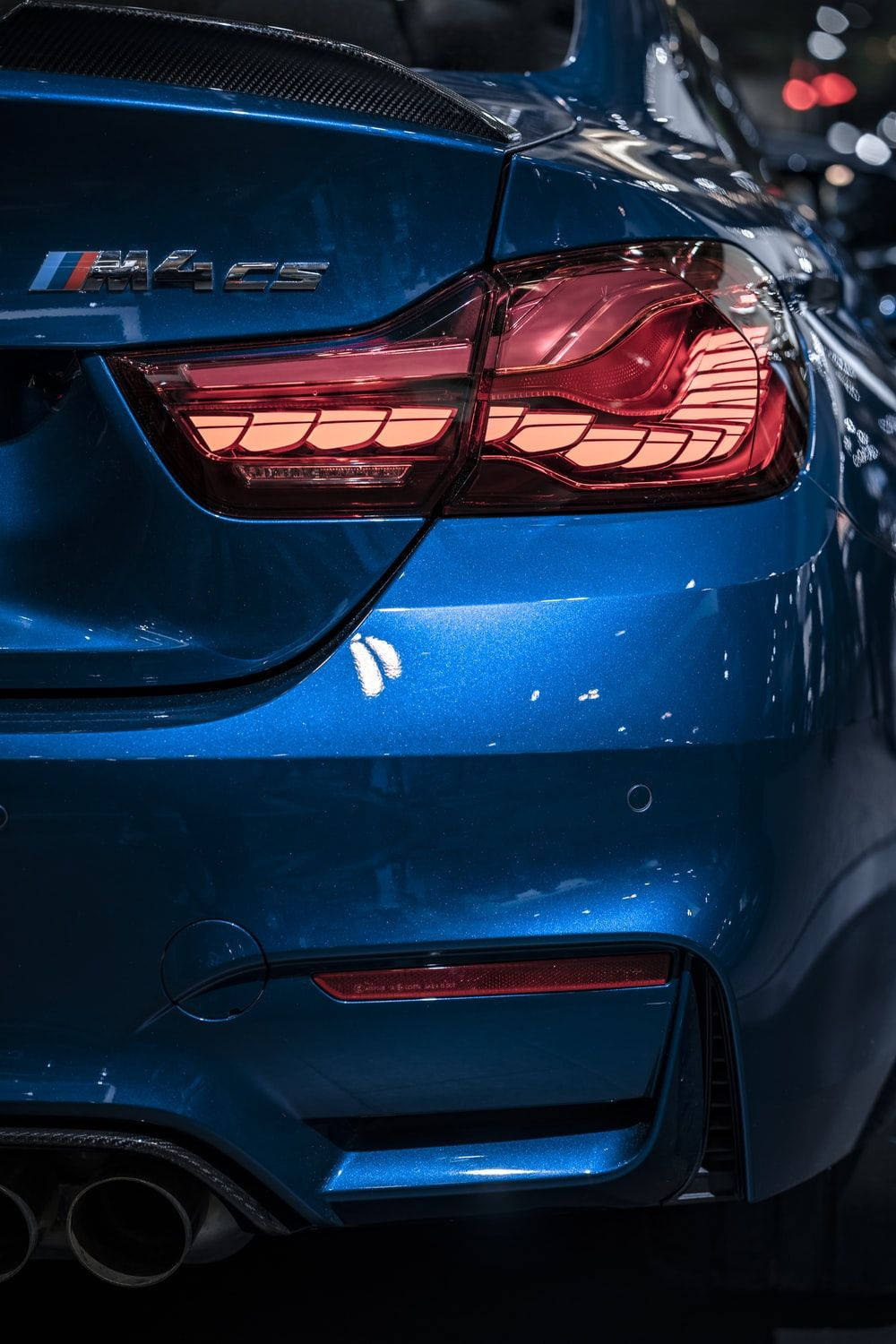 藍色BMW M4尾燈特寫 壁紙 — 鮮藍色BMW M4 CS跑車的特寫，在環境燈光下展示其時尚的尾燈和碳纖維細節。