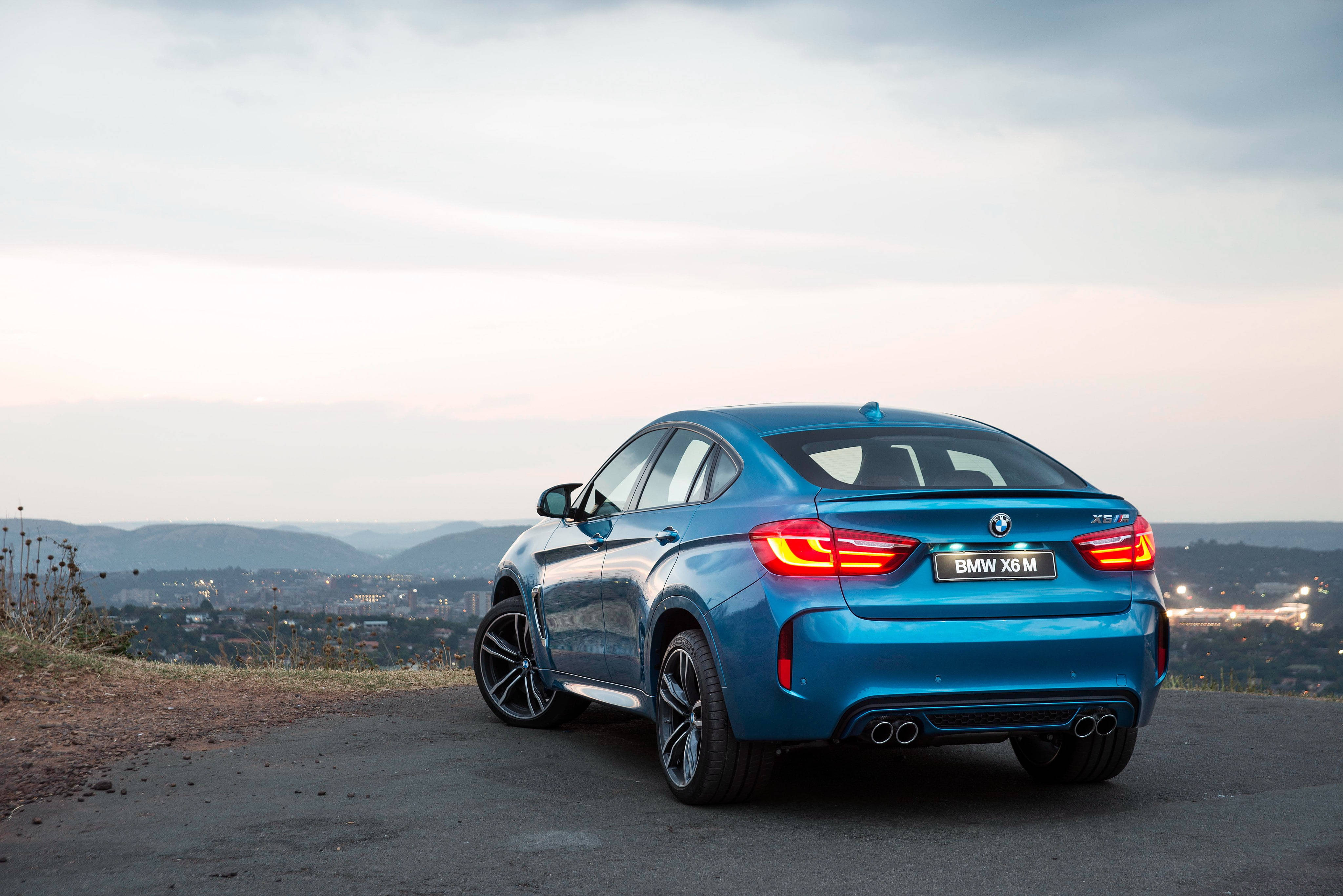 藍色BMW X6 M俯瞰城市 壁紙 — 一輛充滿活力的藍色BMW X6M運動轎跑車停在山頂上，俯瞰著黃昏時分廣闊的城市景觀。