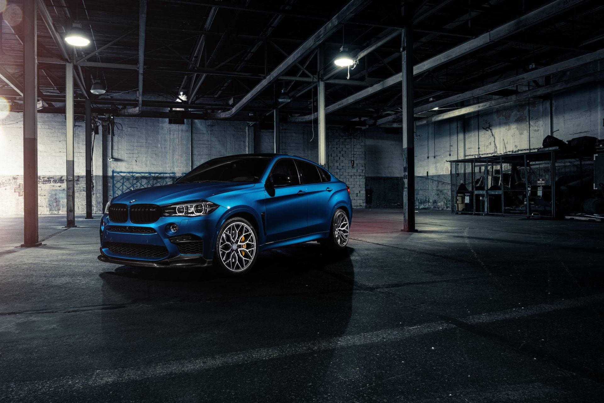 藍色BMW X6 M停於空曠建築內 壁紙 — 一架亮藍色BMW X6 M停泊在光線昏暗的工業車庫，車庫有外露橫樑和混凝土牆。