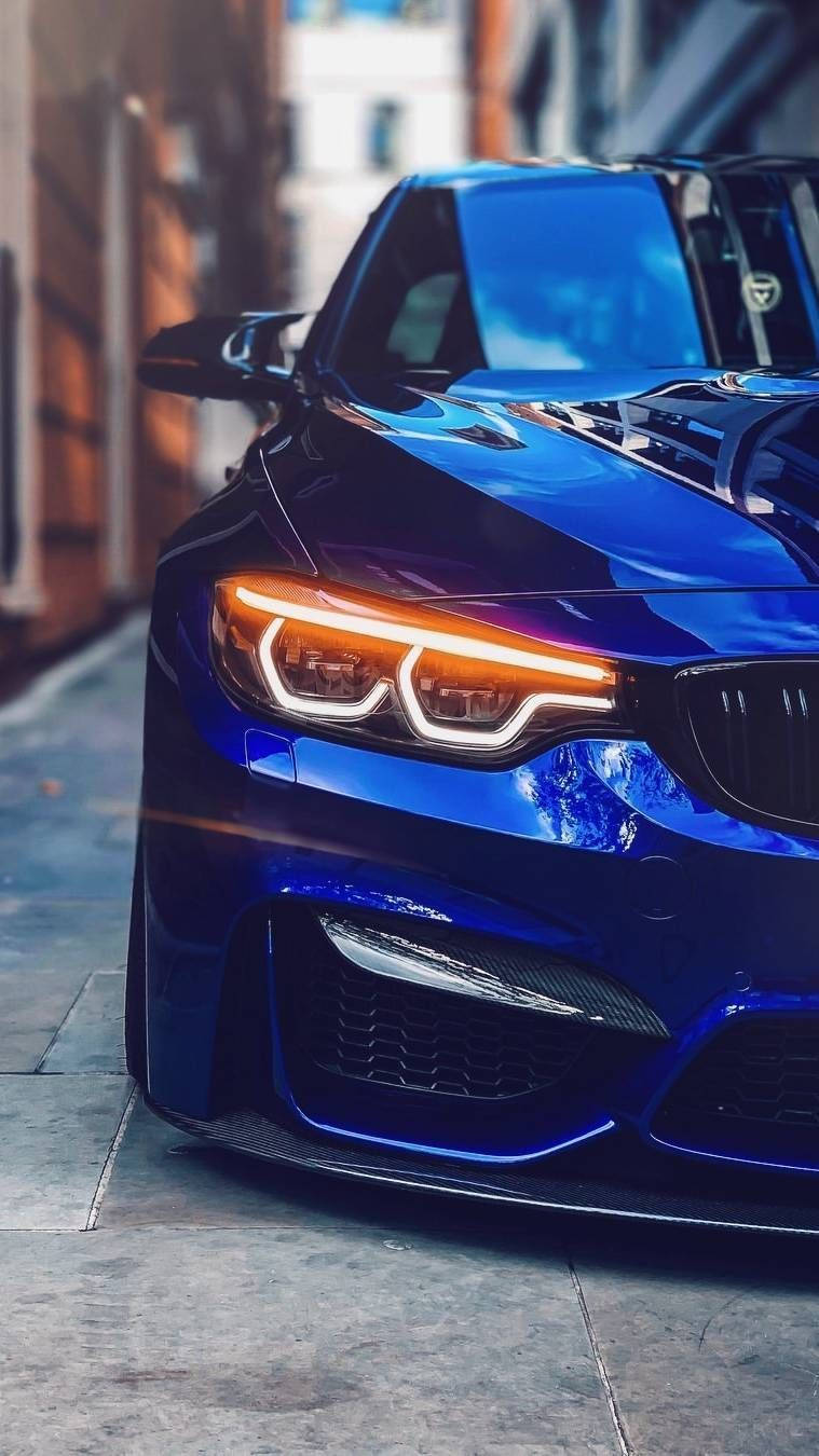 藍色BMW停泊於巷弄之間 壁紙 — 一輛閃亮的藍色跑車，帶有發光的車頭燈，停在一條狹窄的城市街道上。