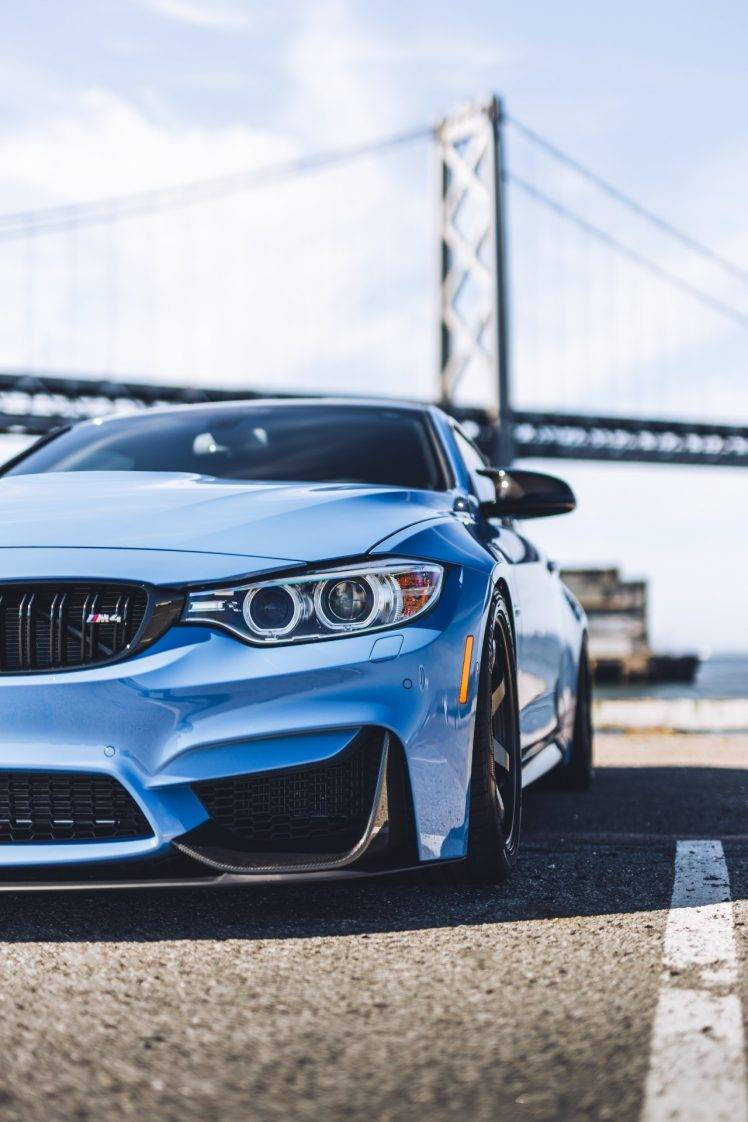 藍色BMW停泊於海灣橋景 壁紙 — 一架時尚的藍色BMW M4跑車停泊在道路上，背景是懸索橋，天空晴朗。