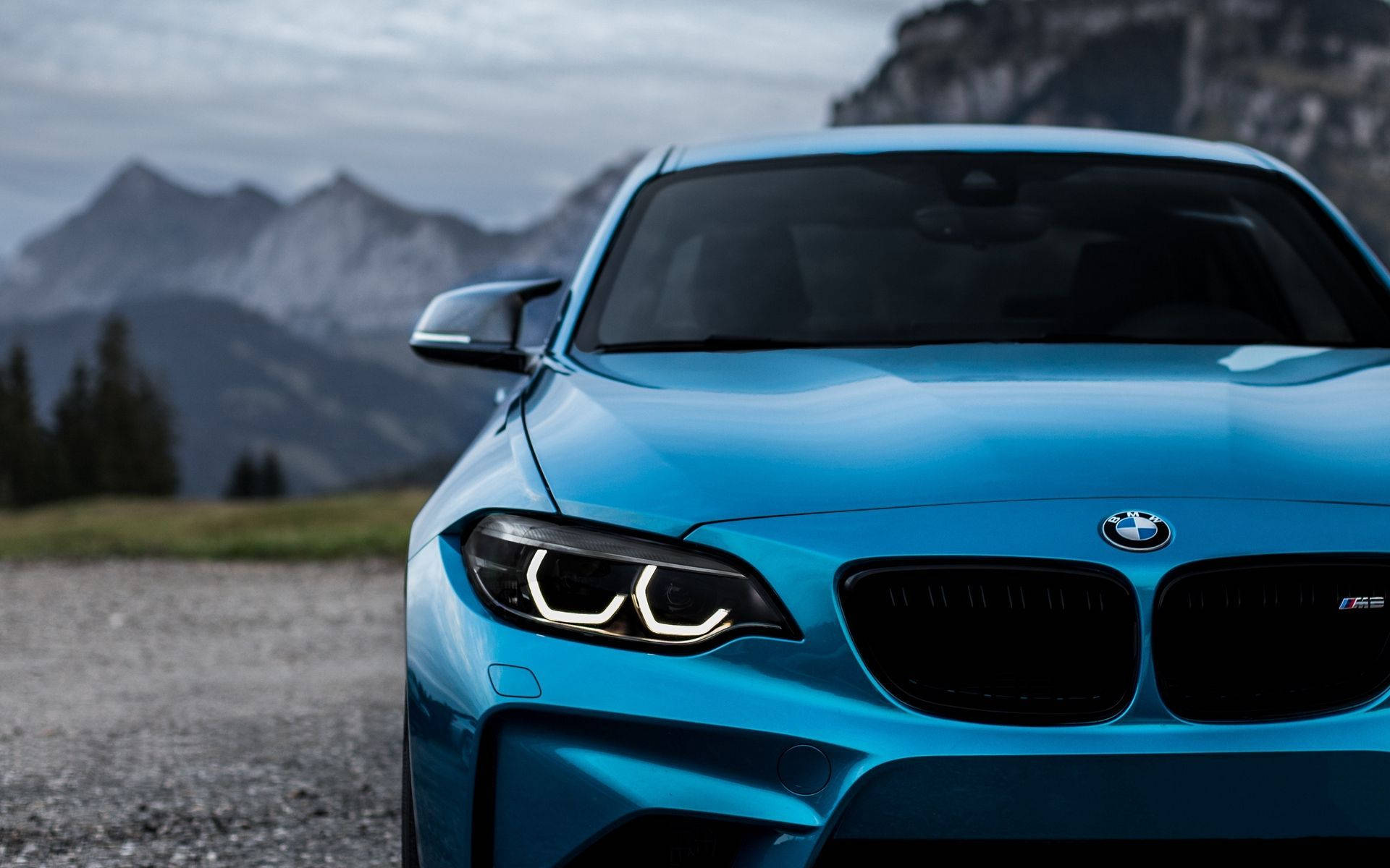 藍色BMW後方山景 壁紙 — 一架充滿活力的藍色BMW M2跑車停泊在碎石路上，背景是霧氣籠罩的山巒。