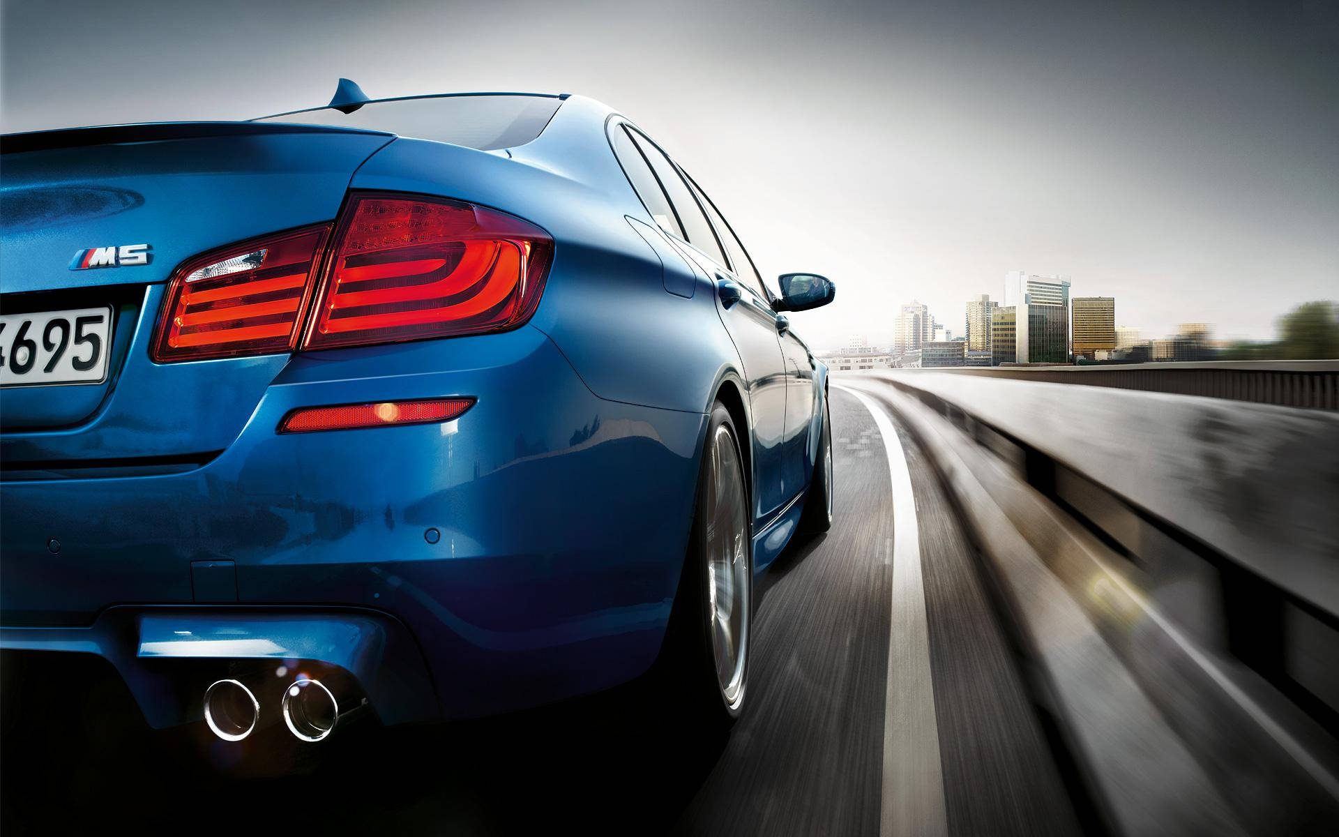 藍色BMW駛向城市 壁紙 — 一輛充滿活力的藍色BMW M5跑車在高速公路上飛馳，遠處是模糊的城市天際線。