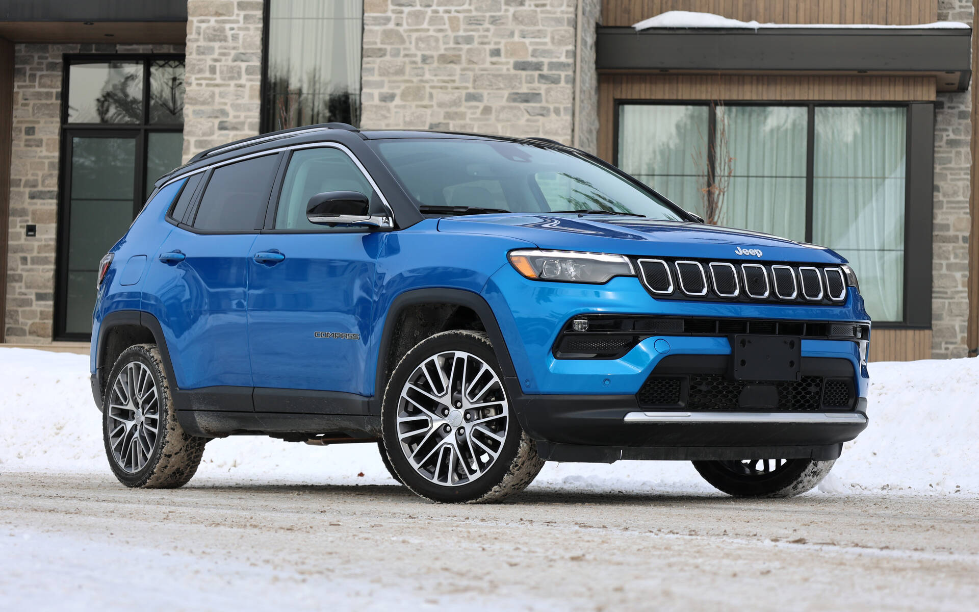 藍色Jeep Compass SUV停泊在現代石建築前，地上有雪。