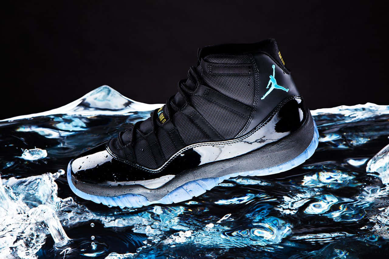 藍色Jordan AJ XI鞋款標誌 壁紙 — 一對黑色Jordan 11波鞋帶有青綠色標誌，從飛濺的冰藍色水中浮現，背景為深色。