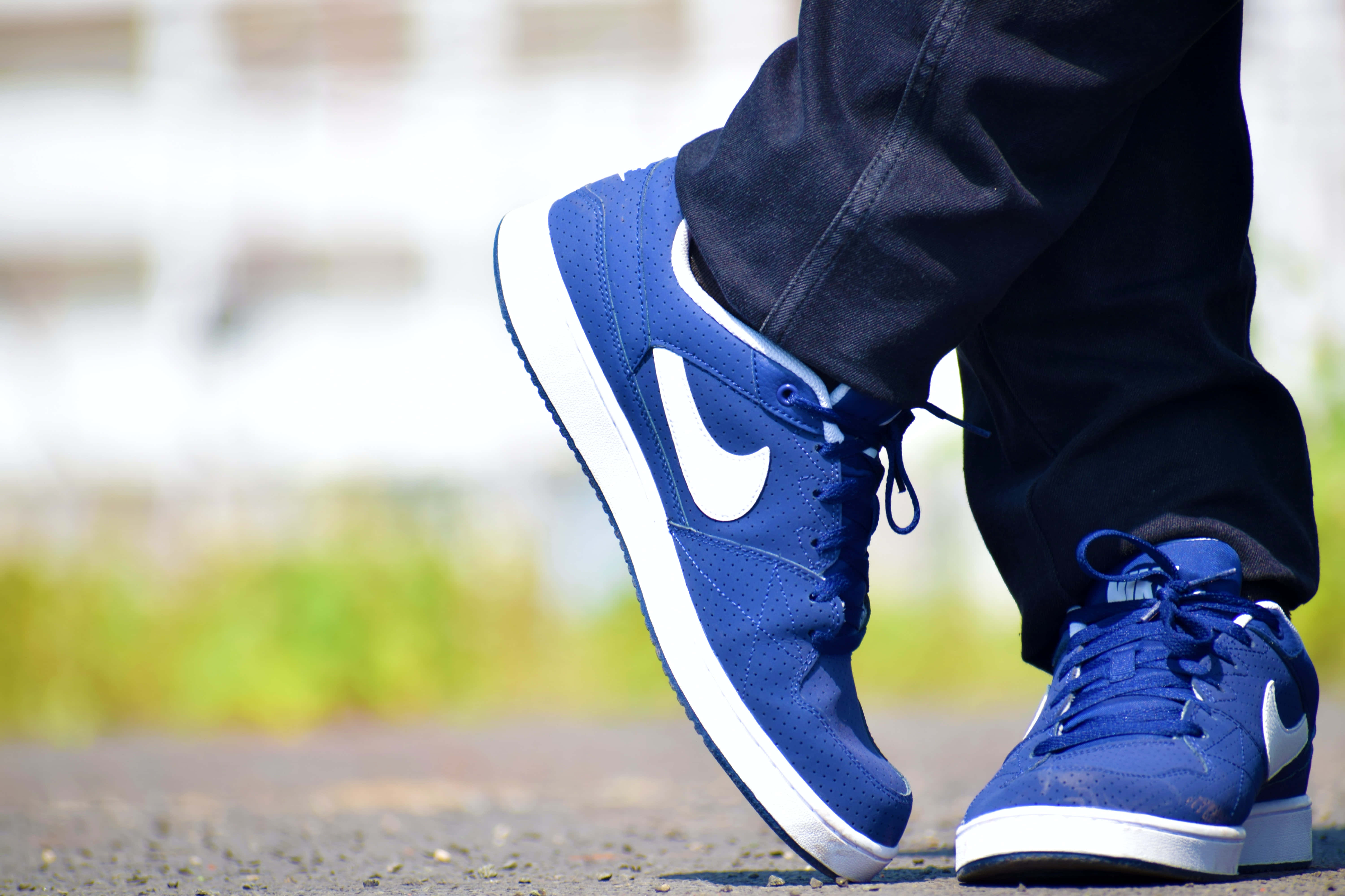 Footwear Design 桌布 壁紙 — 藍色Nike運動鞋特寫，帶白色swoosh標誌，配深色牛仔褲，在碎石路上，明亮日光下。