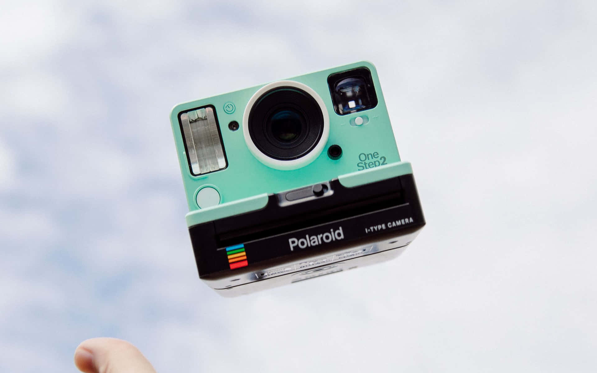 一部薄荷綠色的Polaroid相機漂浮在空中，由一根手指從下方托住。