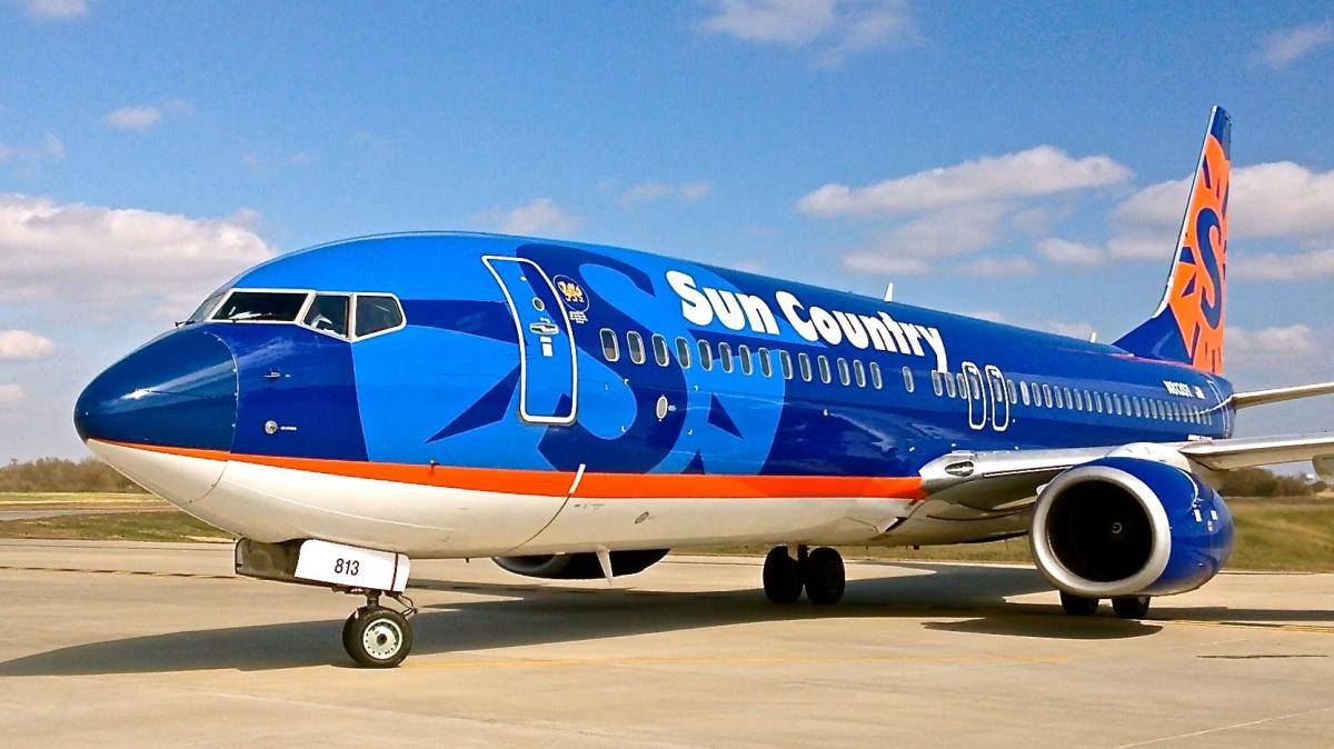 藍色同橙色嘅Sun Country飛機喺晴朗日子停泊喺機場停機坪。