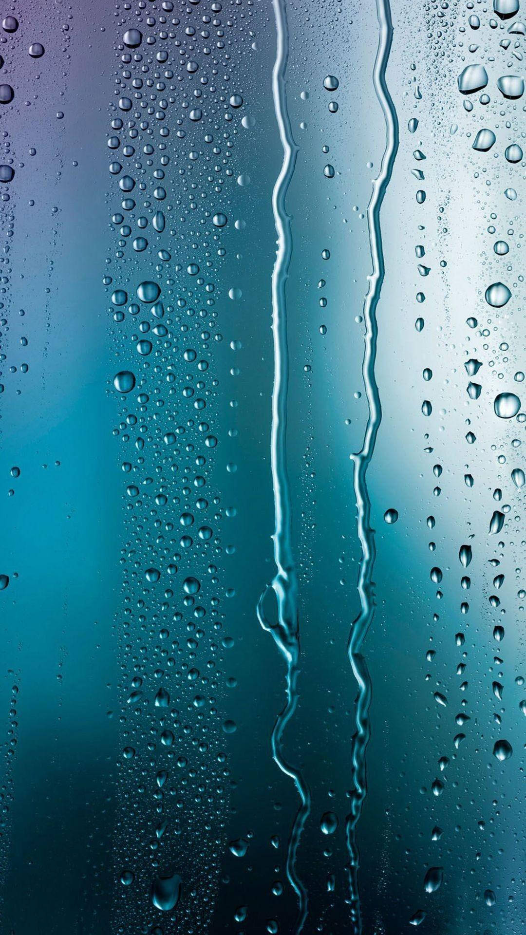 雨滴在帶有青綠色和藍色調的玻璃表面上滑落的特寫。