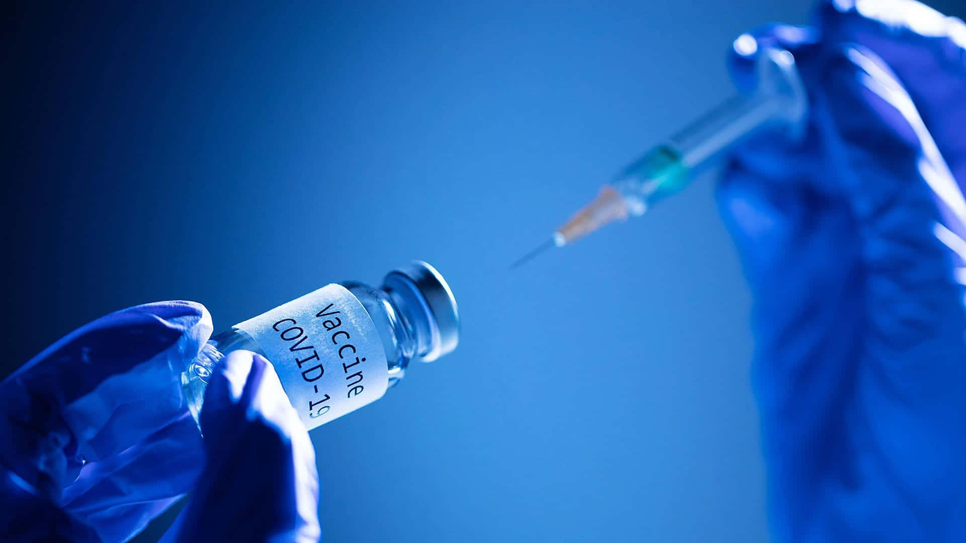 戴藍色手套的手用注射器準備 COVID-19 疫苗。