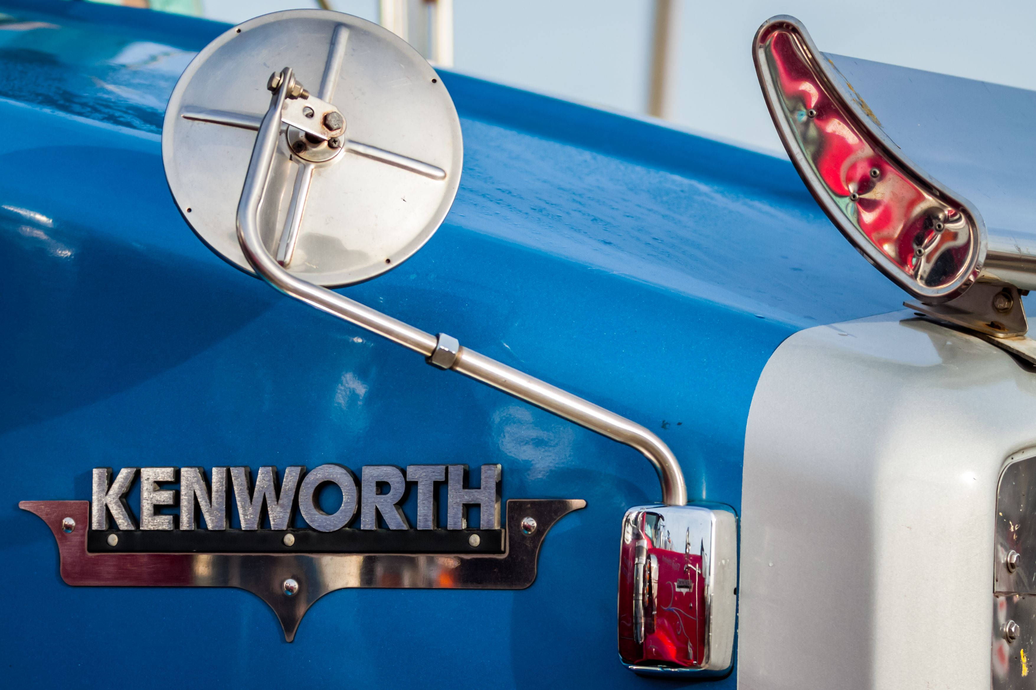 藍色卡車上的肯沃斯標誌 壁紙 — 在明亮日光下，復古藍色 Kenworth 卡車的鍍鉻側鏡和標誌特寫。