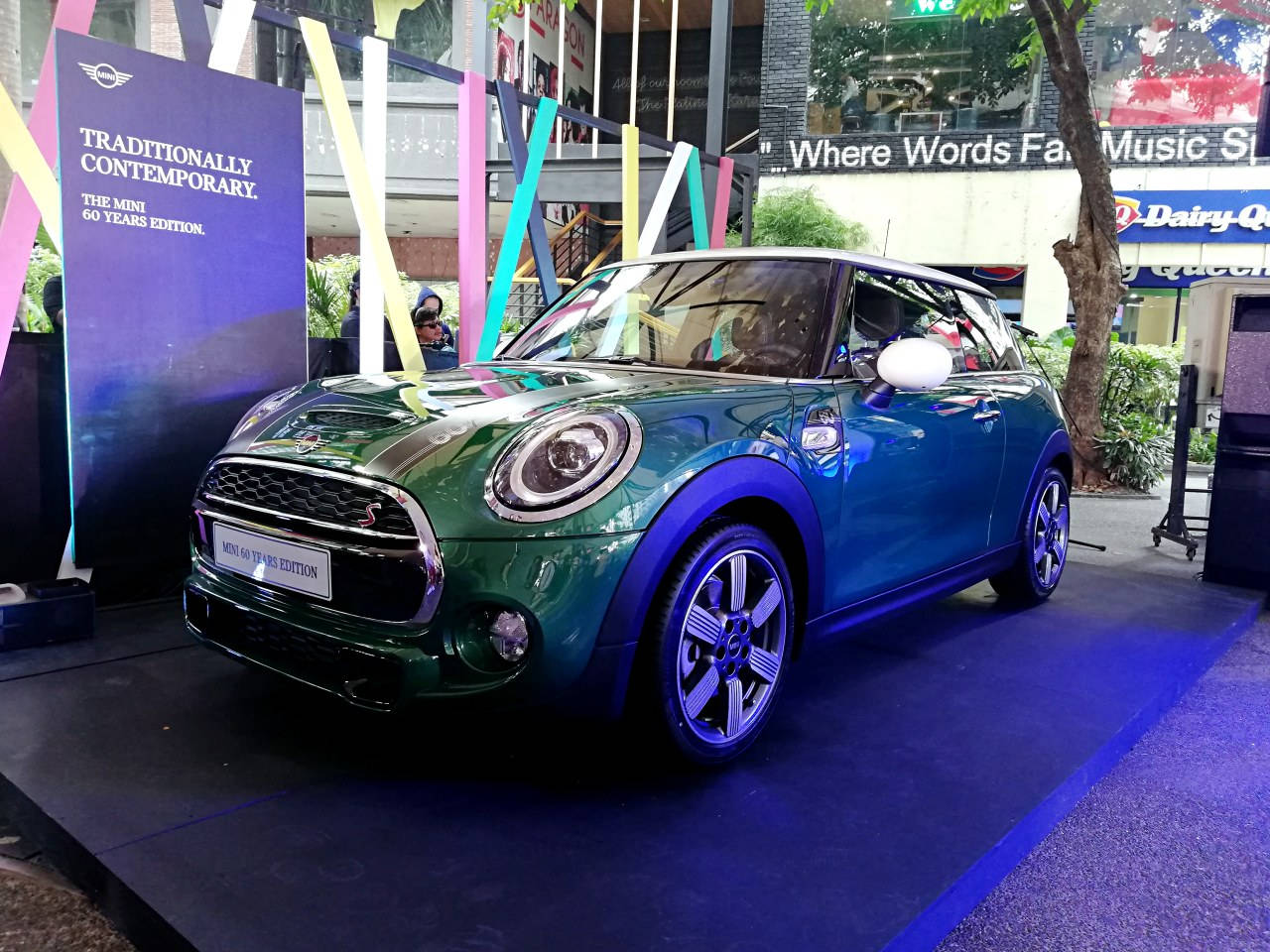 藍色地毯上的藍色美學迷你車 壁紙 — 一輛光澤的綠色MINI Cooper S 60 Years Edition汽車在充滿活力的藍色舞台燈光下，於城市戶外發布活動中閃閃發光。