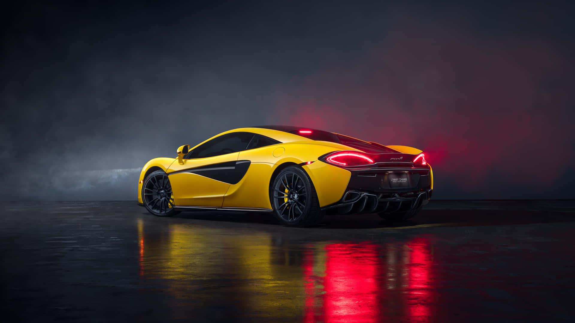 黃色McLaren跑車在煙霧瀰漫的工作室中，紅色尾燈閃爍，地板反射光線。