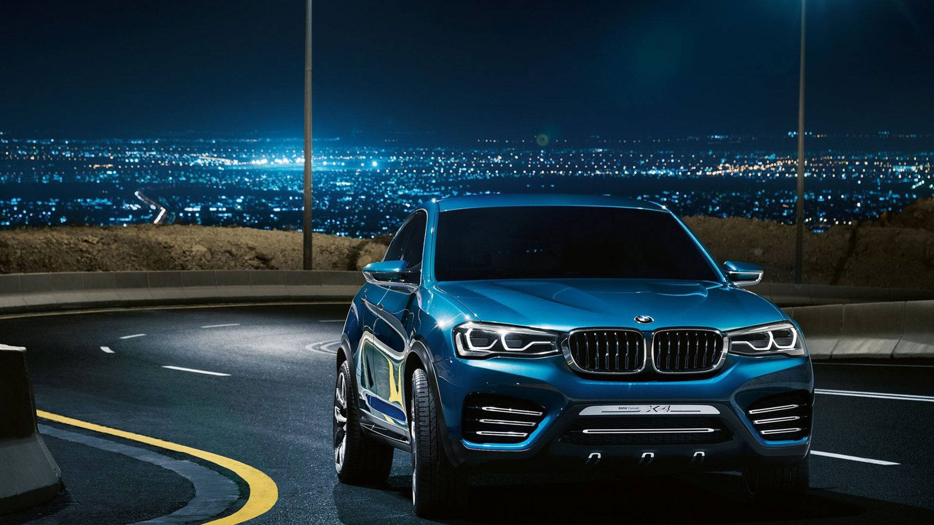 藍色寶馬與城市夜景 壁紙 — 一輛時尚的藍色BMW SUV在夜間沿著蜿蜒的山路行駛，下方是閃爍的城市景觀。