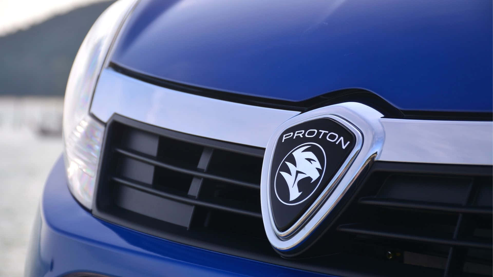 Proton 桌布 壁紙 — 藍色寶騰汽車前格柵的特寫，其鍍鉻標誌在模糊的戶外背景下展示。