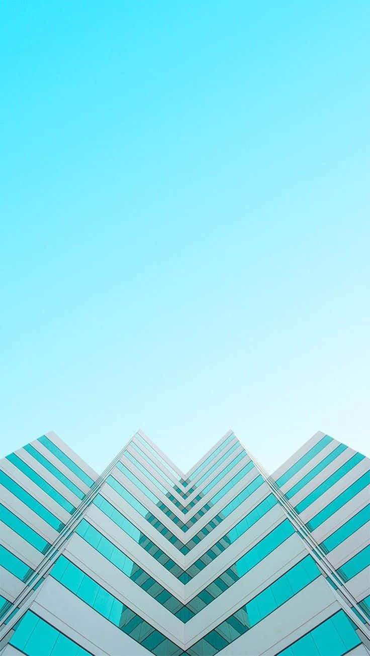 藍色建築極簡iPhone壁紙 壁紙 — 現代玻璃摩天大樓，帶有青綠色窗戶，在晴朗的青色天空下以低角度城市拍攝中聳立。