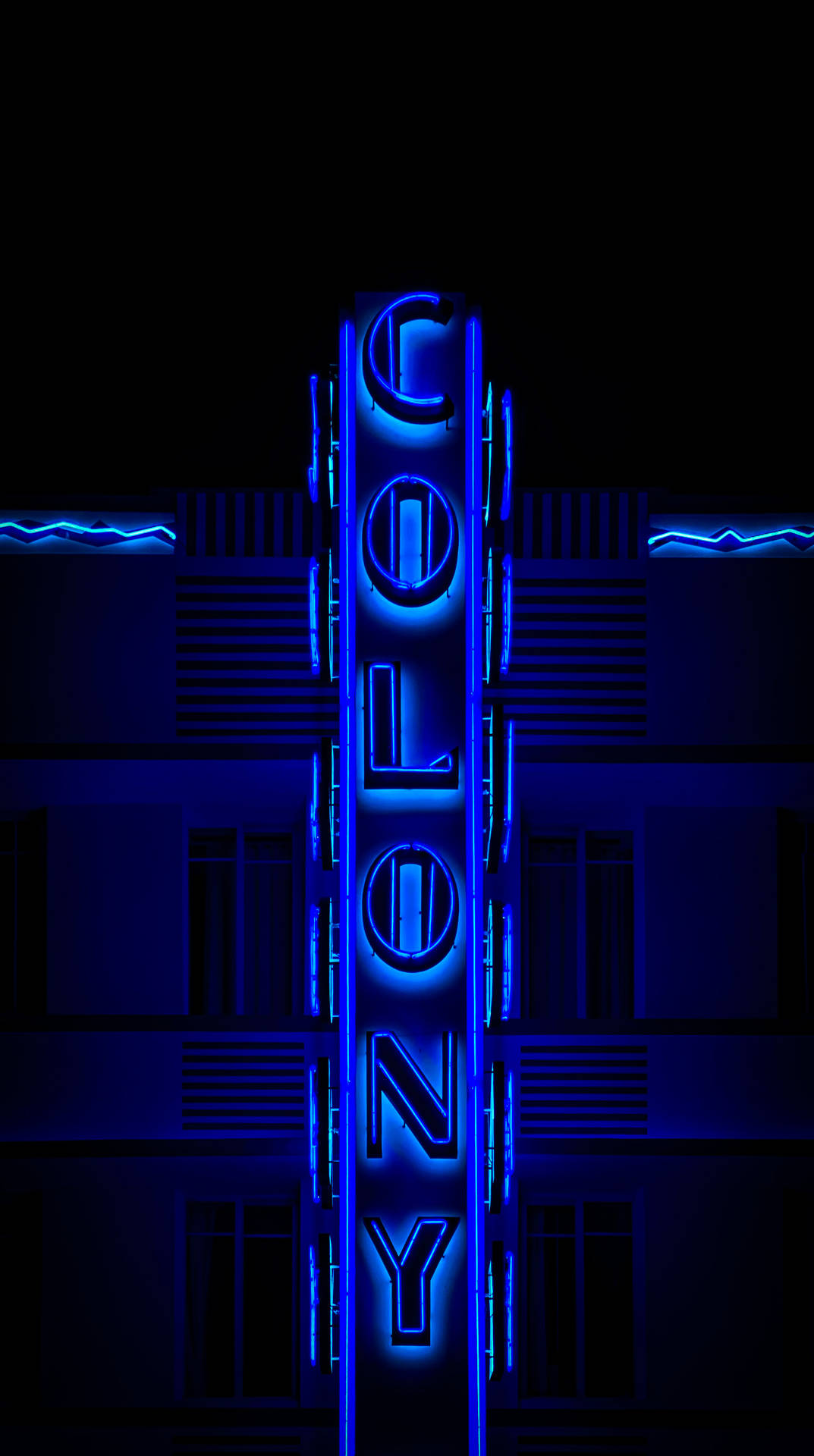 夜晚，黑暗建築物上的藍色霓虹燈牌，上面寫著COLONY。