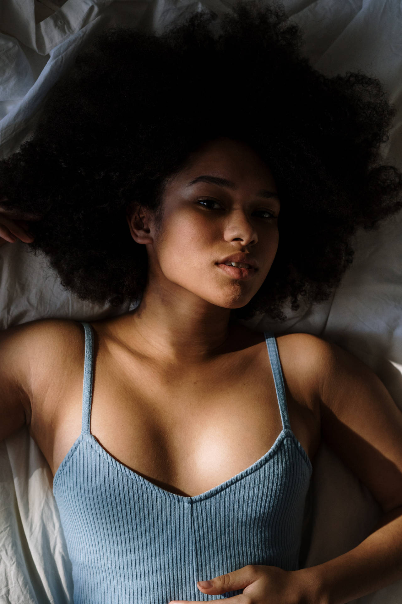 一位捲髮女性穿著藍色上衣在床上休息。