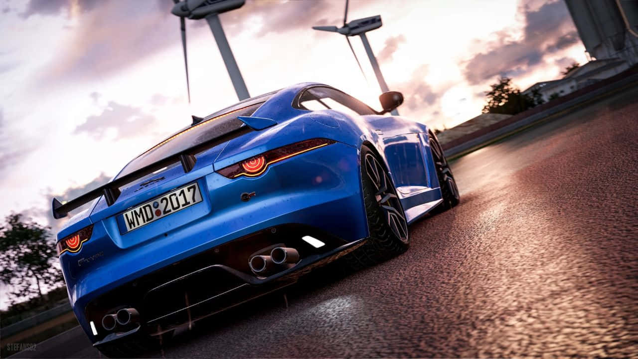 藍色捷豹運動車 720p Project Cars 背景 壁紙 — 一輛充滿活力的藍色跑車，發光的尾燈在日落時分沿著潮濕的賽道飛馳，背景是風力發電機。