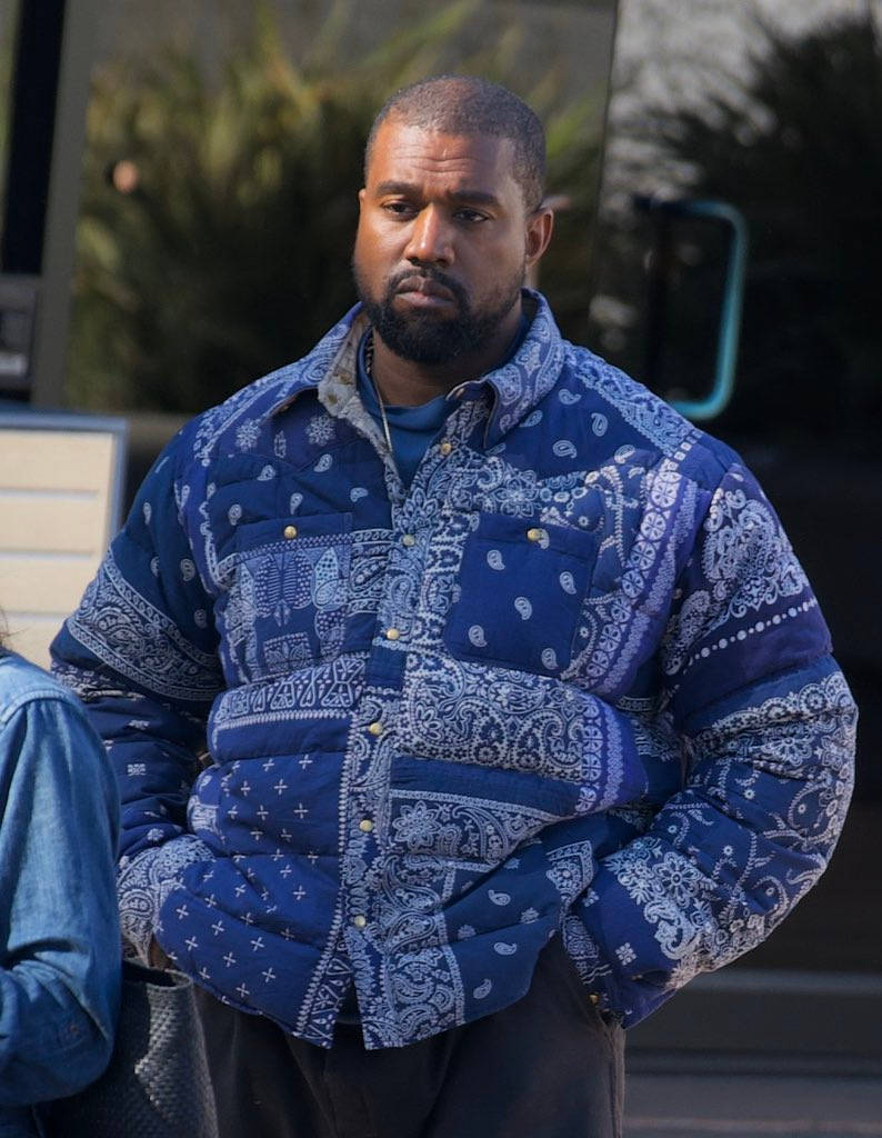 藍色方巾夾克的坎耶·威斯特 壁紙 — Kanye West 喺戶外企喺度，著住一件搶眼嘅藍色佩斯利絎縫外套，雙手插喺袋入面。