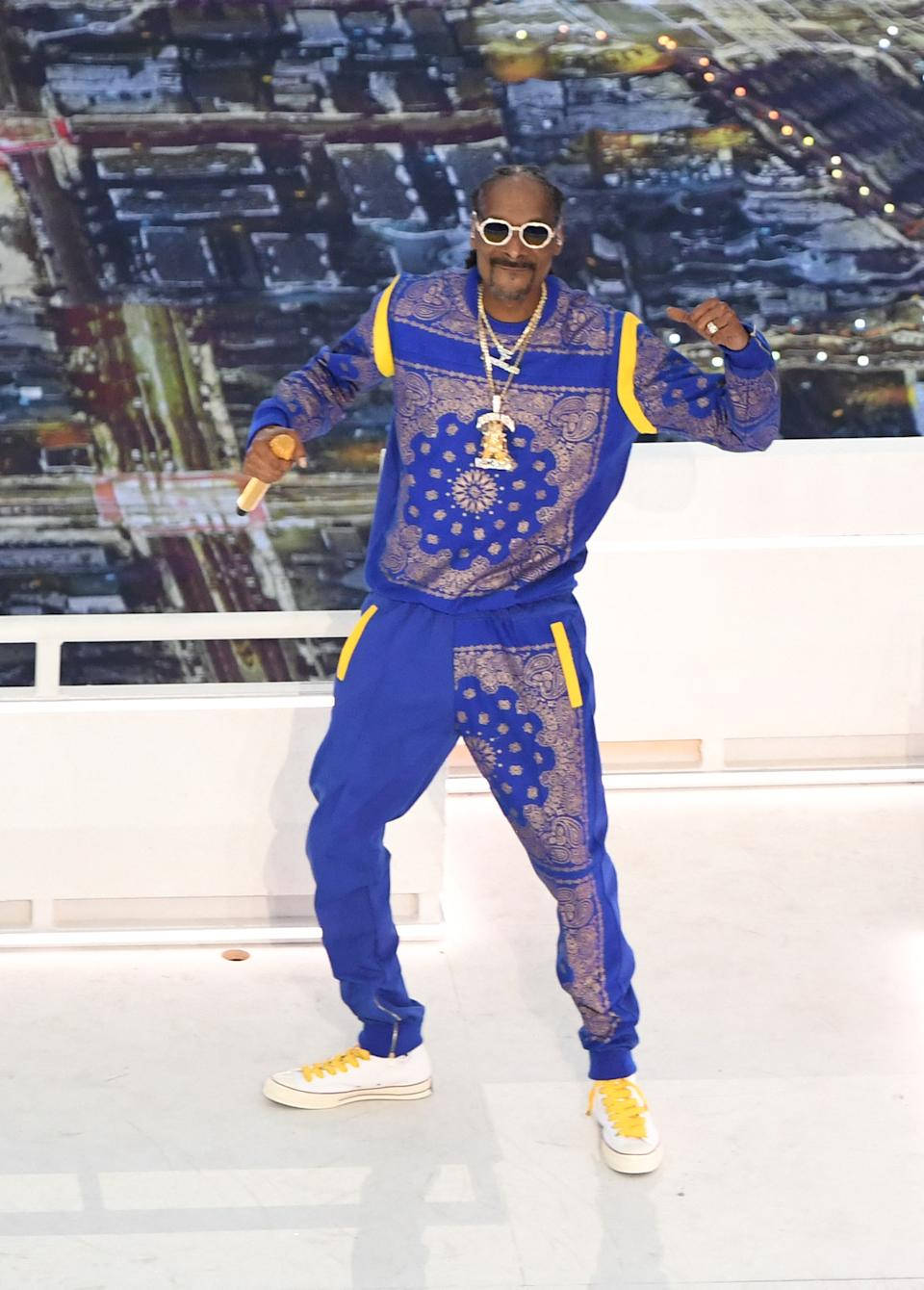 藍色方巾服裝的史努比·道格 壁紙 — Snoop Dogg 身穿大膽的藍黃圖案運動服，在屋頂舞台上自信擺姿勢，身後是城市燈光。