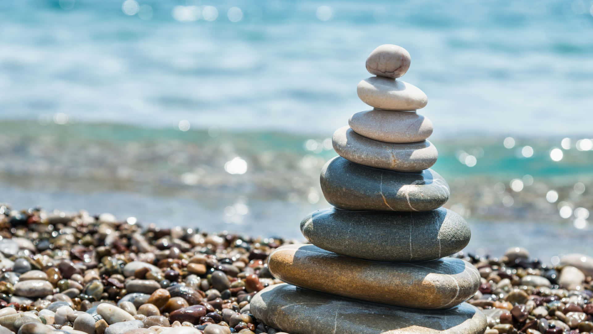 卵石海灘上堆疊的石頭，背景是閃爍的海浪。