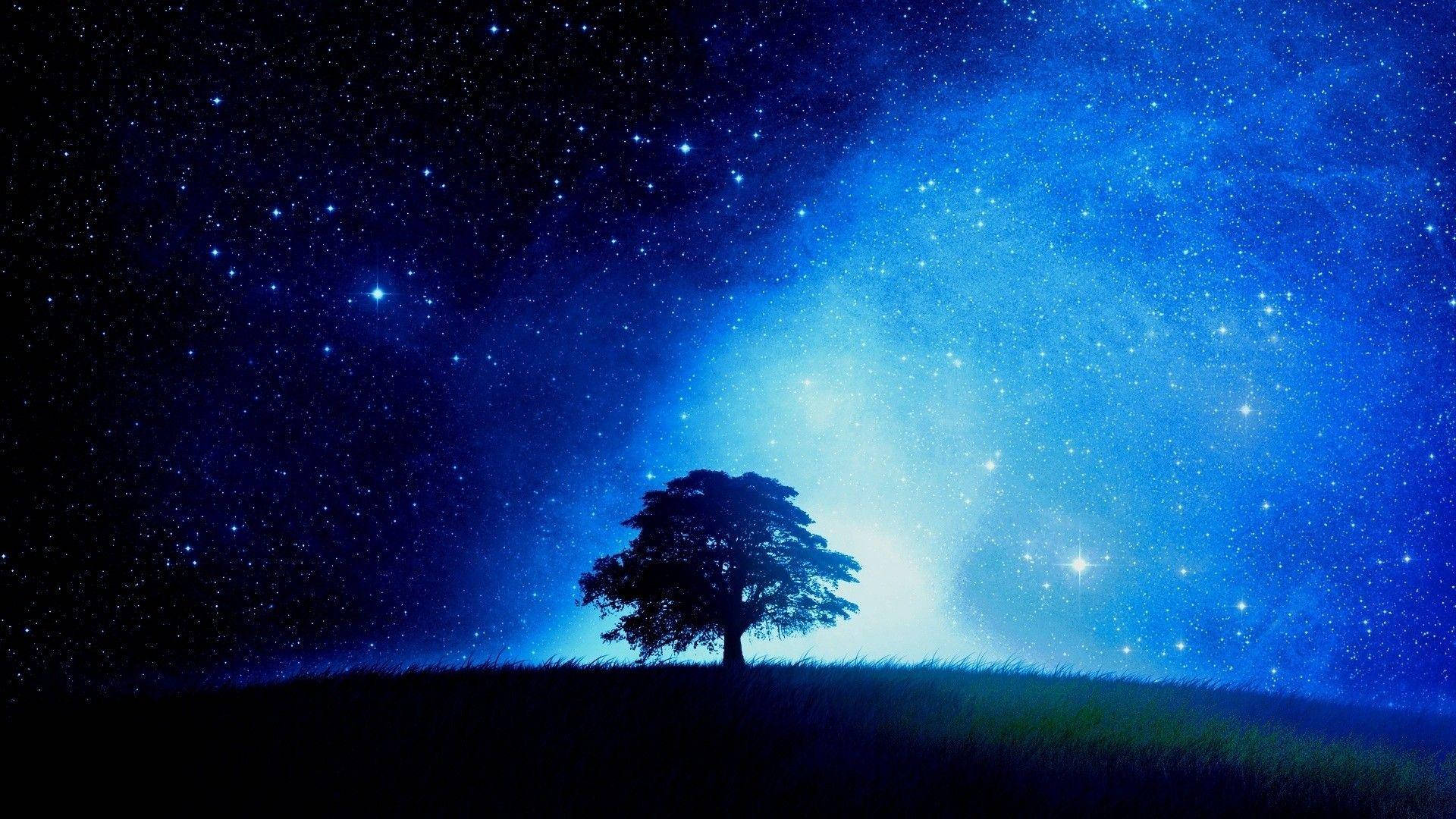 藍色星系與繁星夜空 壁紙 — 一棵孤獨的樹在長滿草的山丘上形成剪影，背景是廣闊的星空夜空，散發著宇宙藍光。