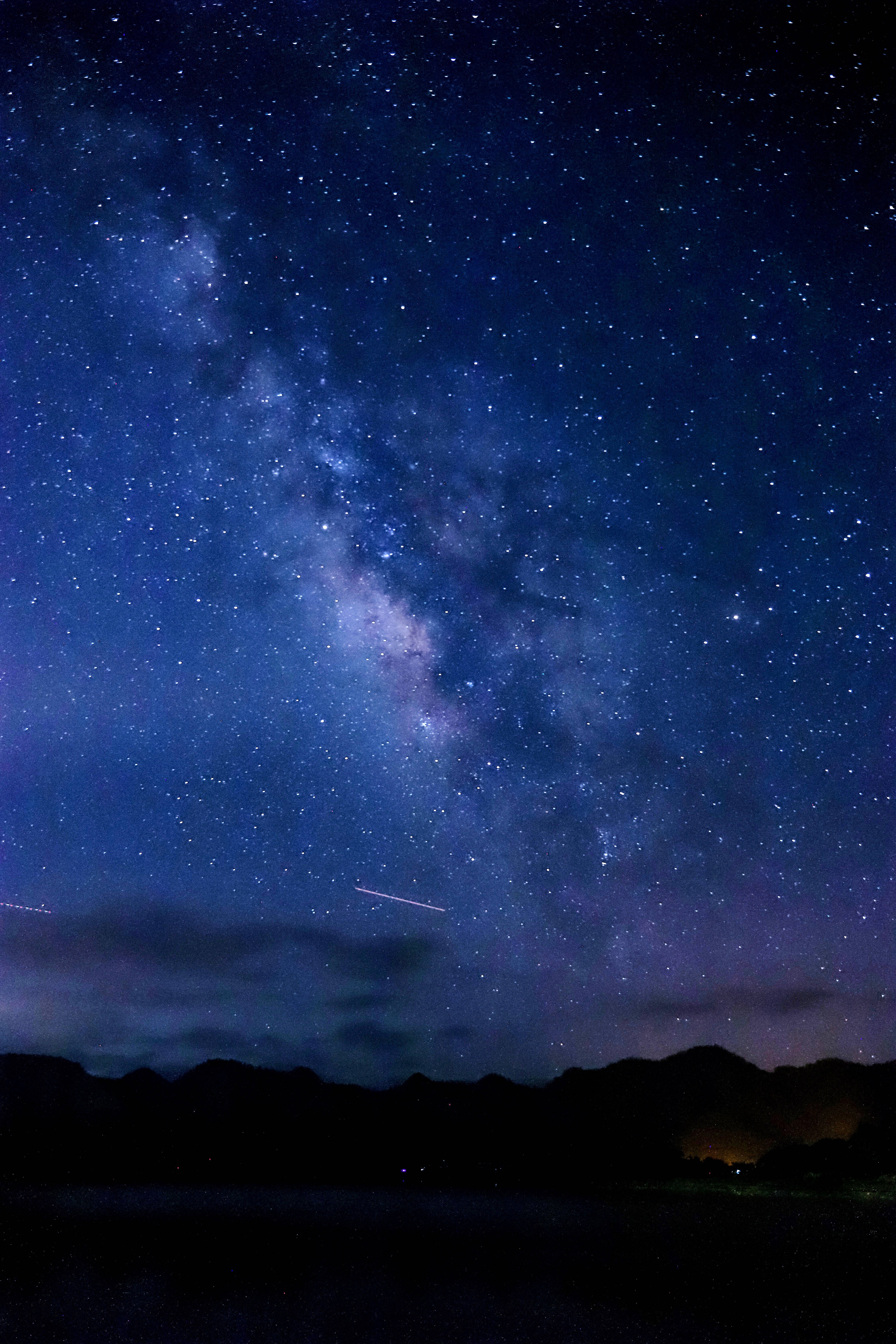 藍色星系閃爍夜空 壁紙 — 一個令人屏息的夜空，充滿無數星星，閃爍的銀河在黑暗的山脈剪影和寧靜的湖泊上方拱起。