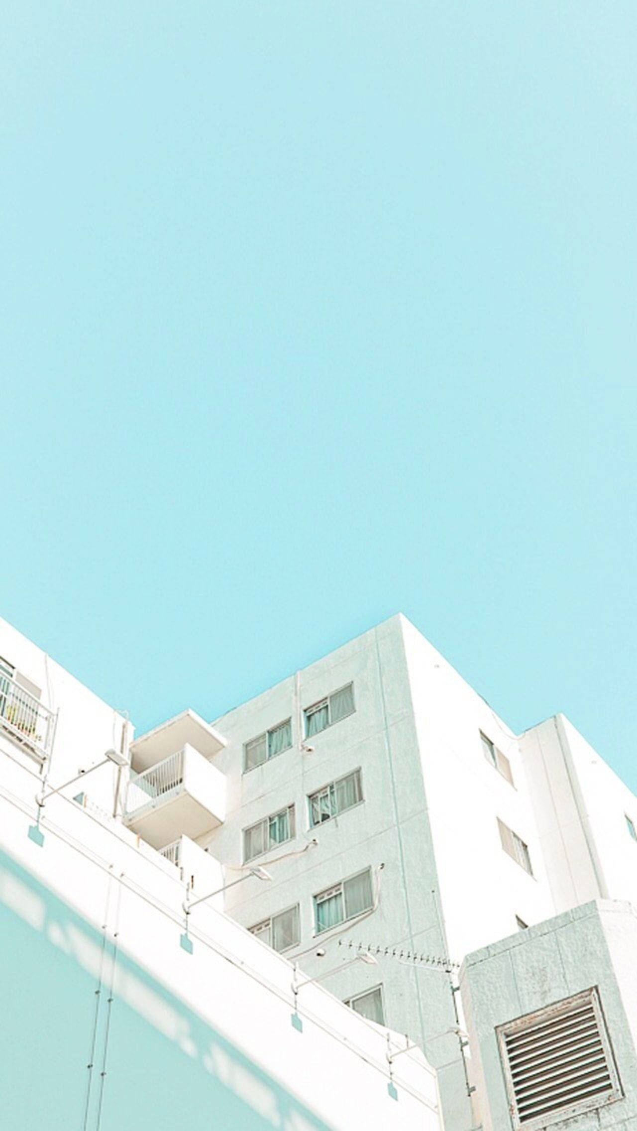 藍色柔霧風情白色建築 壁紙 — 低角度拍攝白色公寓大樓，背景是廣闊清澈的青色天空，帶有柔和陰影。