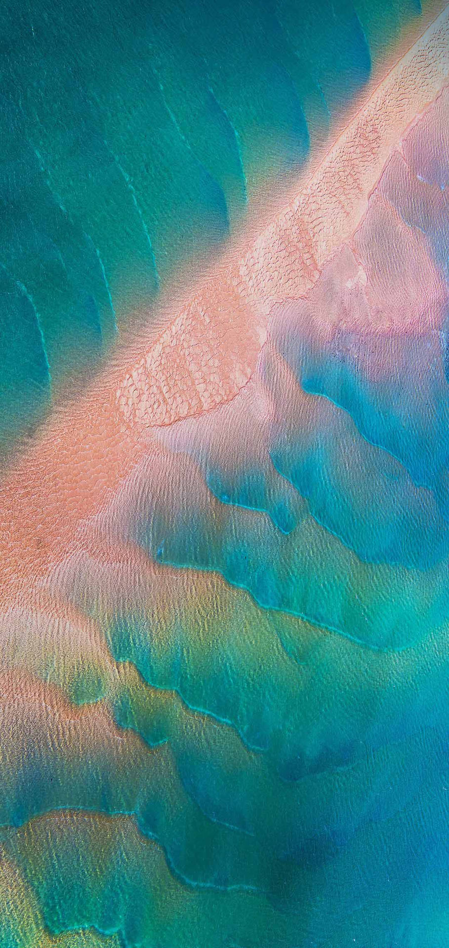 從空中俯瞰，海浪與粉紅色沙灘相遇，形成色彩繽紛的漸變圖案。