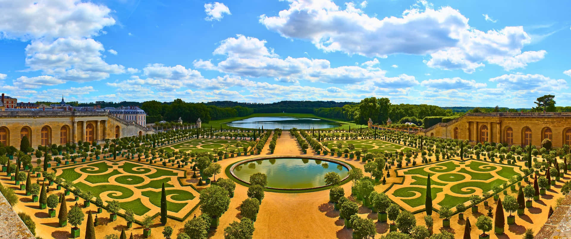 大型正式花園，幾何樹籬和中央池塘，在晴朗的天空下。