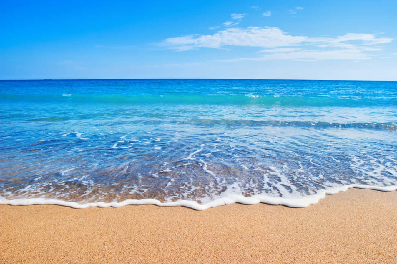 藍色海浪與沙灘畫面 壁紙 — 平靜的藍綠色海浪輕輕地拍打著金色的沙灘，天空湛藍，飄著幾縷薄雲。