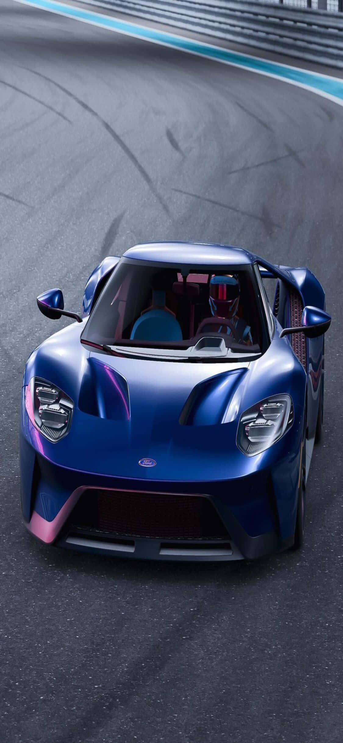 藍色福特 GT iPhone X《Forza Motorsport 7》背景 壁紙 — 一輛帶有粉紅色點綴的亮藍色跑車在賽道上奔馳，賽道上有可見的輪胎痕跡和藍白相間的賽道邊緣。