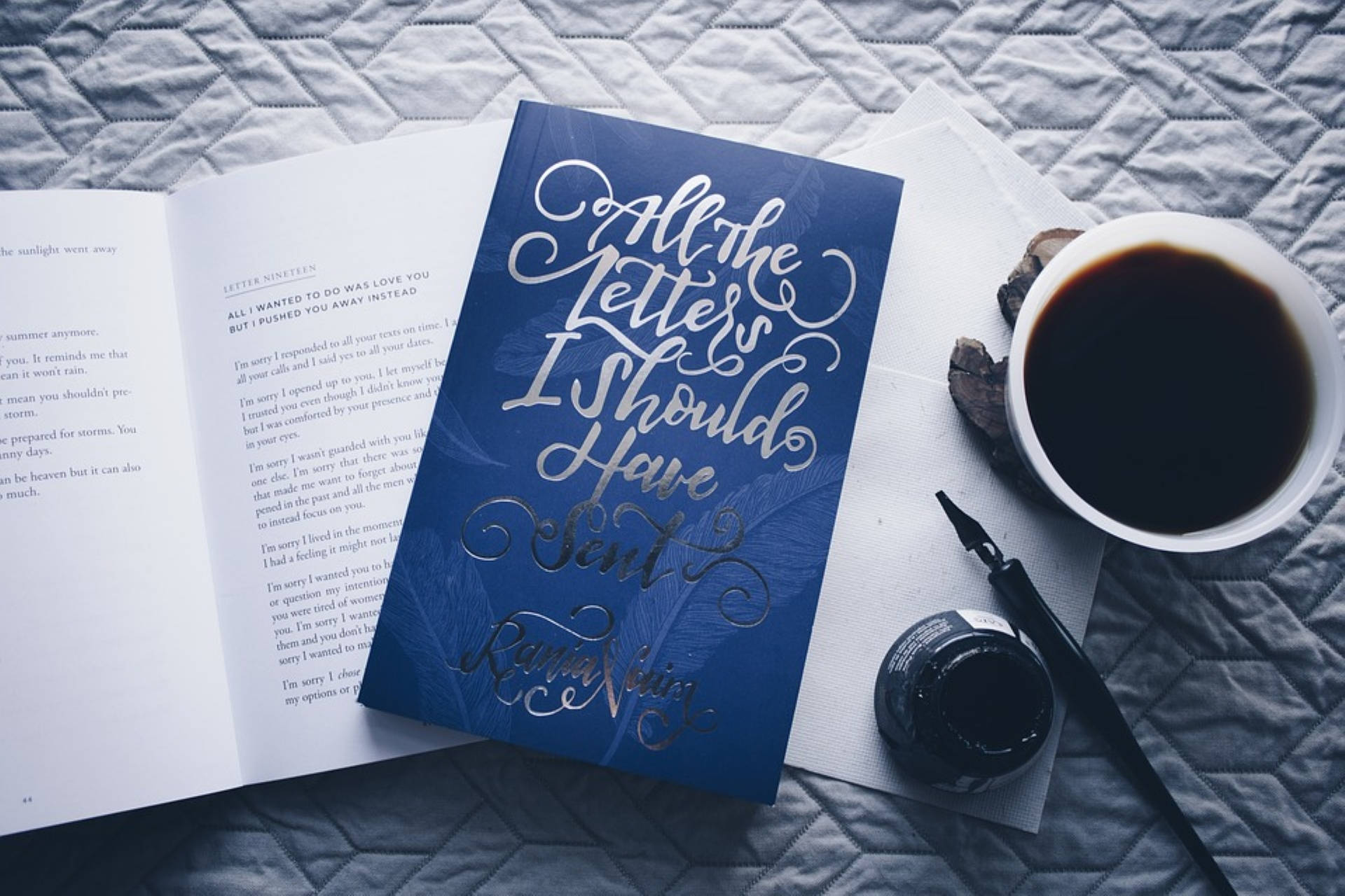 藍色系書本與咖啡 壁紙 — 一本名為《All the Letters I Should Have Sent》的藍色書本打開著，旁邊放著一杯咖啡和一支鋼筆，置於絎縫灰色表面上。