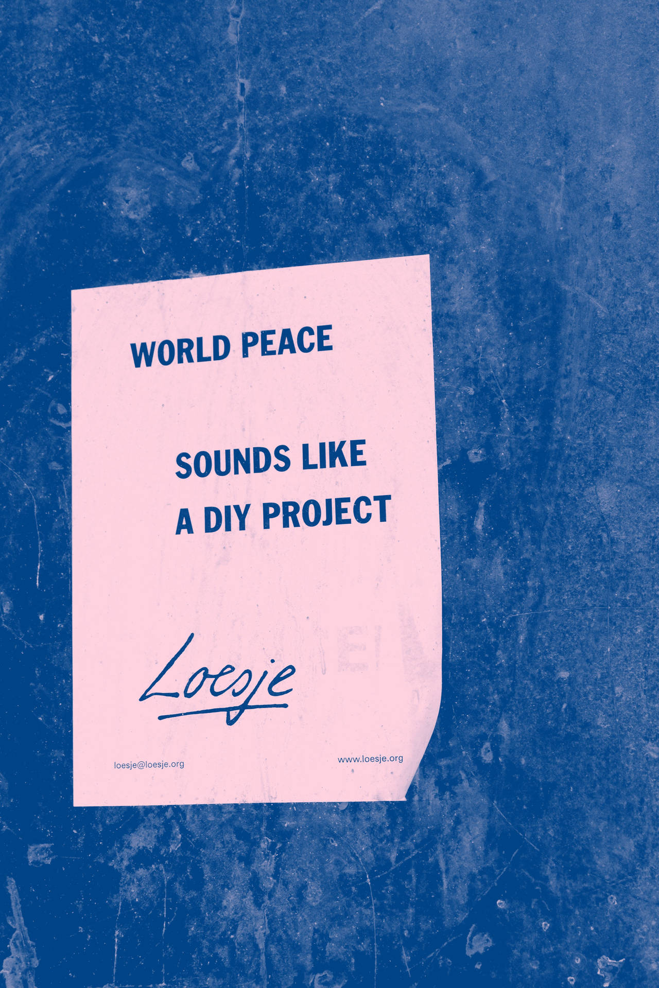 藍色牆上的粉紅色便條，寫著「World Peace Sounds Like a DIY Project」並有簽名。