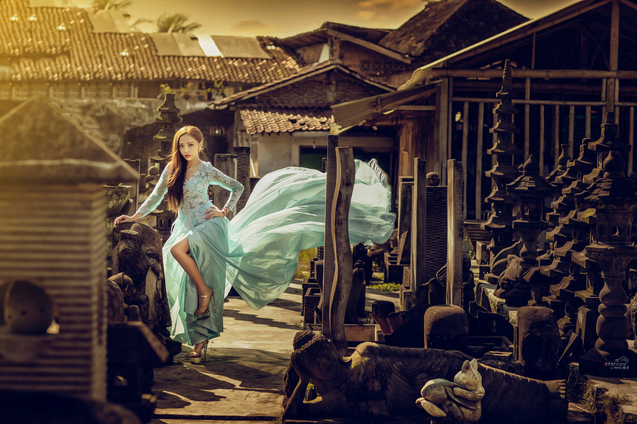 藍色蕾絲禮服 壁紙 — 一位身穿飄逸青綠色連衣裙的女性，在溫暖的金色陽光下，優雅地在風化的木結構中擺姿勢。