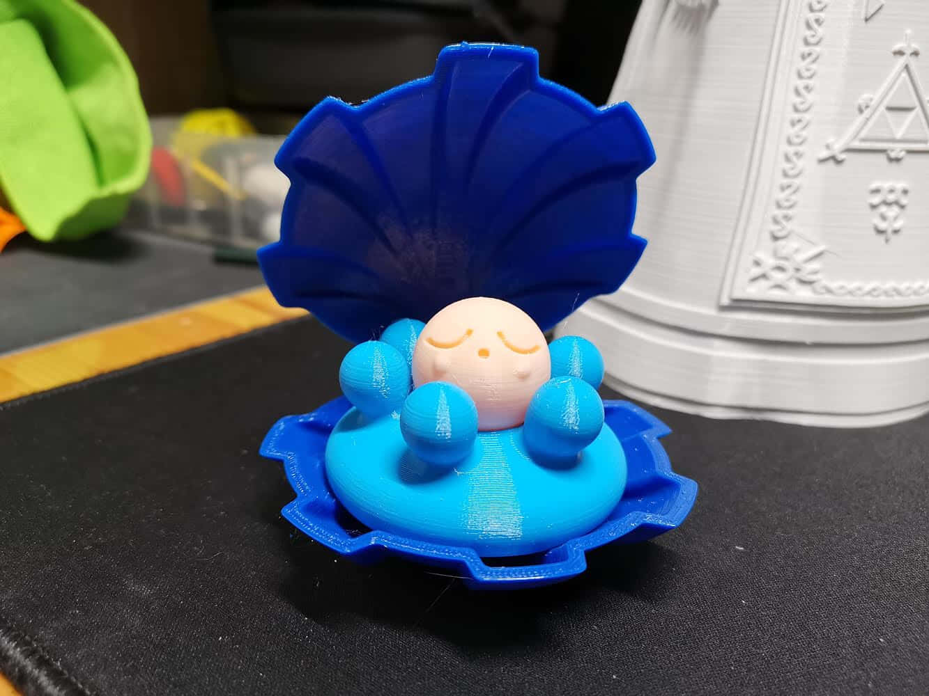 一個藍色3D打印的貝殼玩具，裡面有一顆微笑的珍珠。