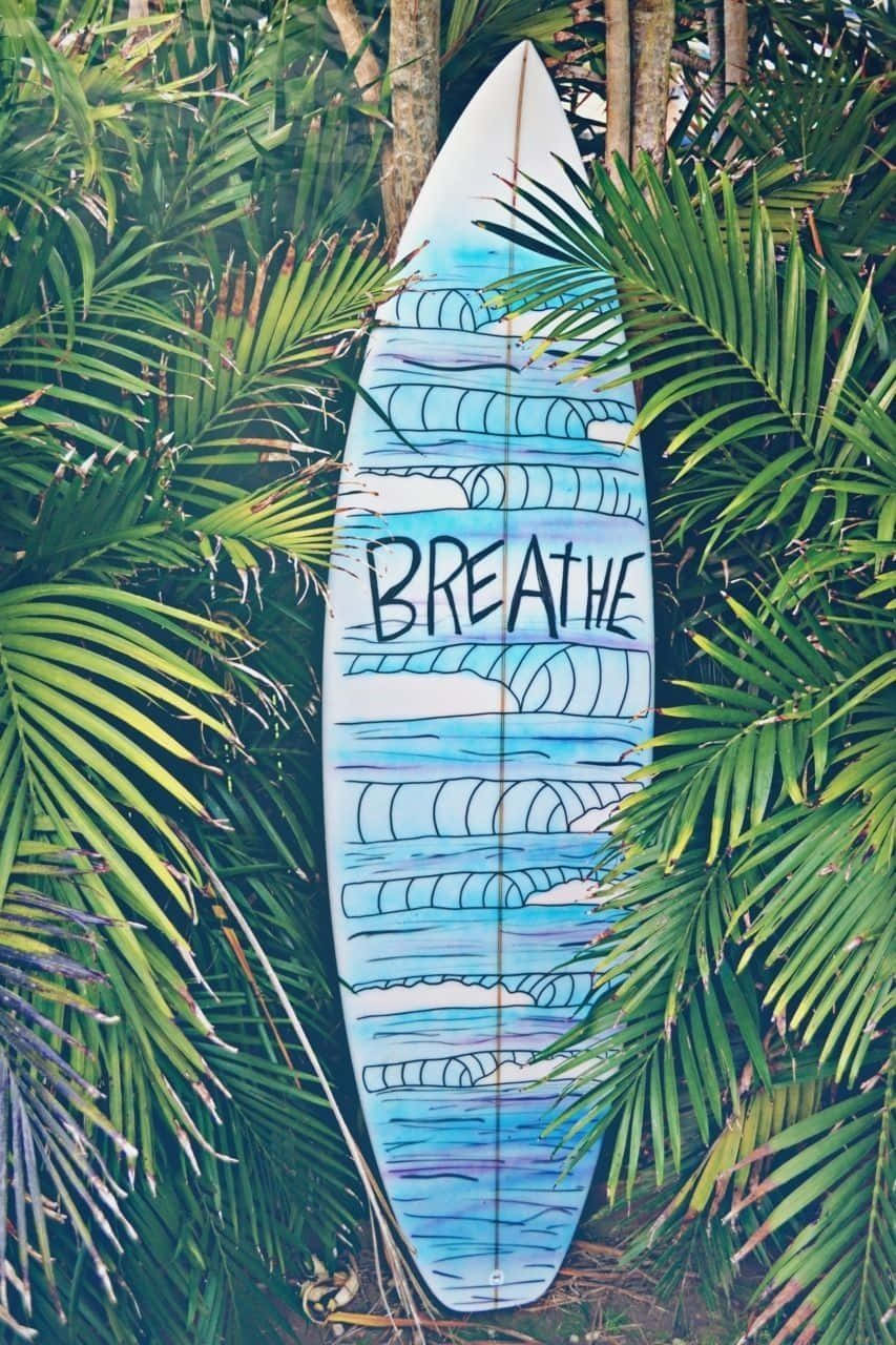 一塊裝飾有 breathe 字樣的衝浪板立在棕櫚葉之間。