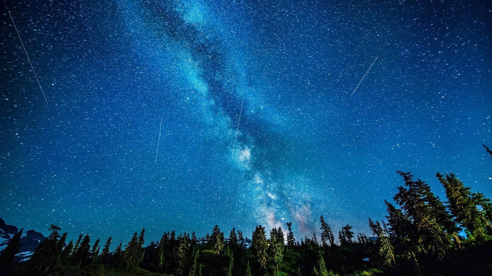 銀河系在夜晚的森林和山脈上方發光。
