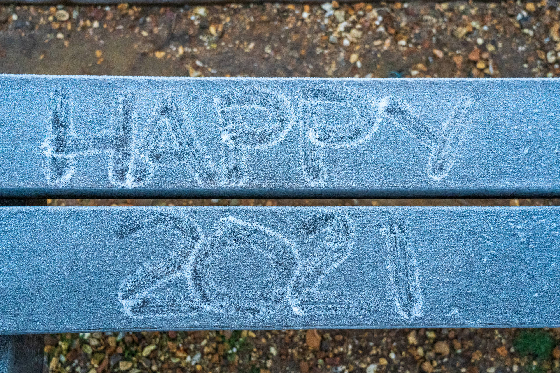 結霜的長椅，碎石路上用粉筆寫著「HAPPY 2021」。