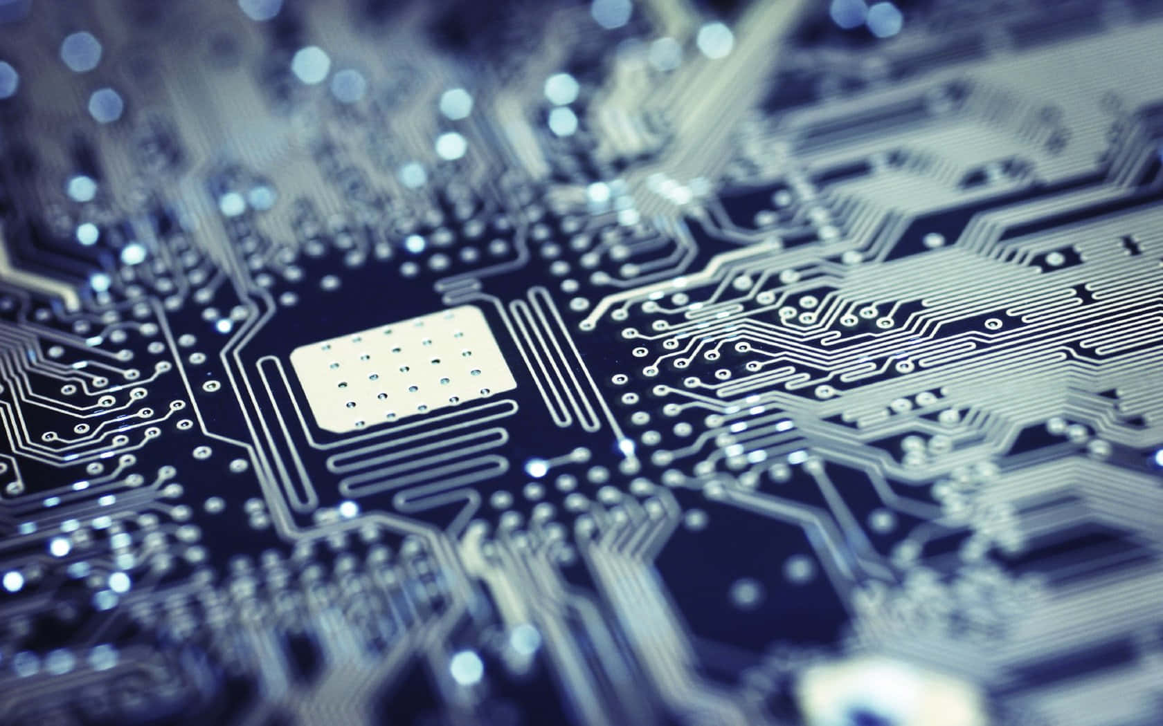 Electronics 桌布 壁紙 — 藍色電路板的特寫微距鏡頭，帶有複雜的銀色路徑和一個中央晶片，在淺景深下柔和發光。