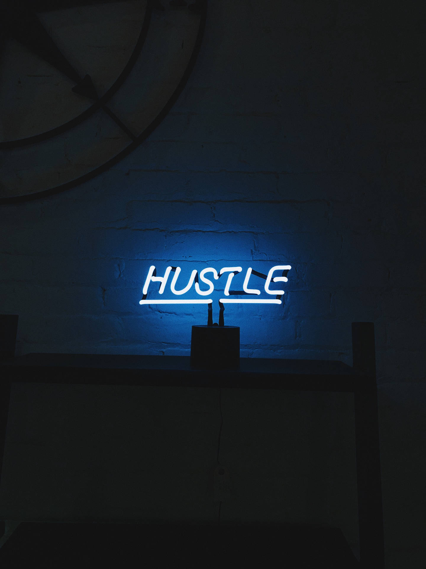 藍色霓虹燈牌，在暗色磚牆上顯示 HUSTLE。