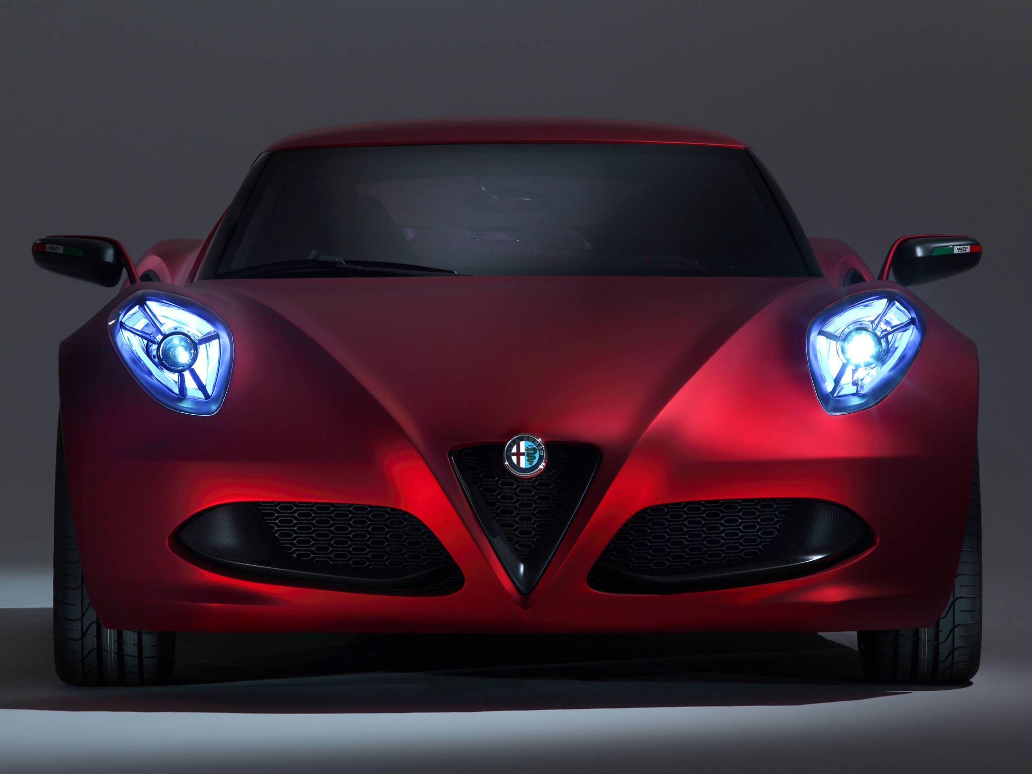 藍色頭燈Alfa Romeo iPhone拍攝 壁紙 — 一輛時尚的紅色阿爾法羅密歐跑車，配備發光的藍色頭燈，在黑暗的攝影棚背景下向前凝視。