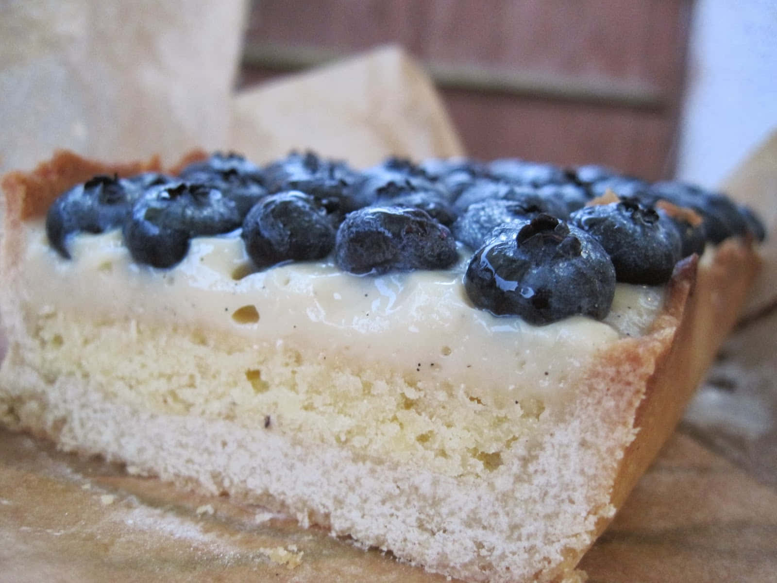 Blueberries Tart 桌布 壁紙 — 藍莓撻一片嘅特寫，有忌廉餡料同金黃色撻皮，放喺牛油紙上面。