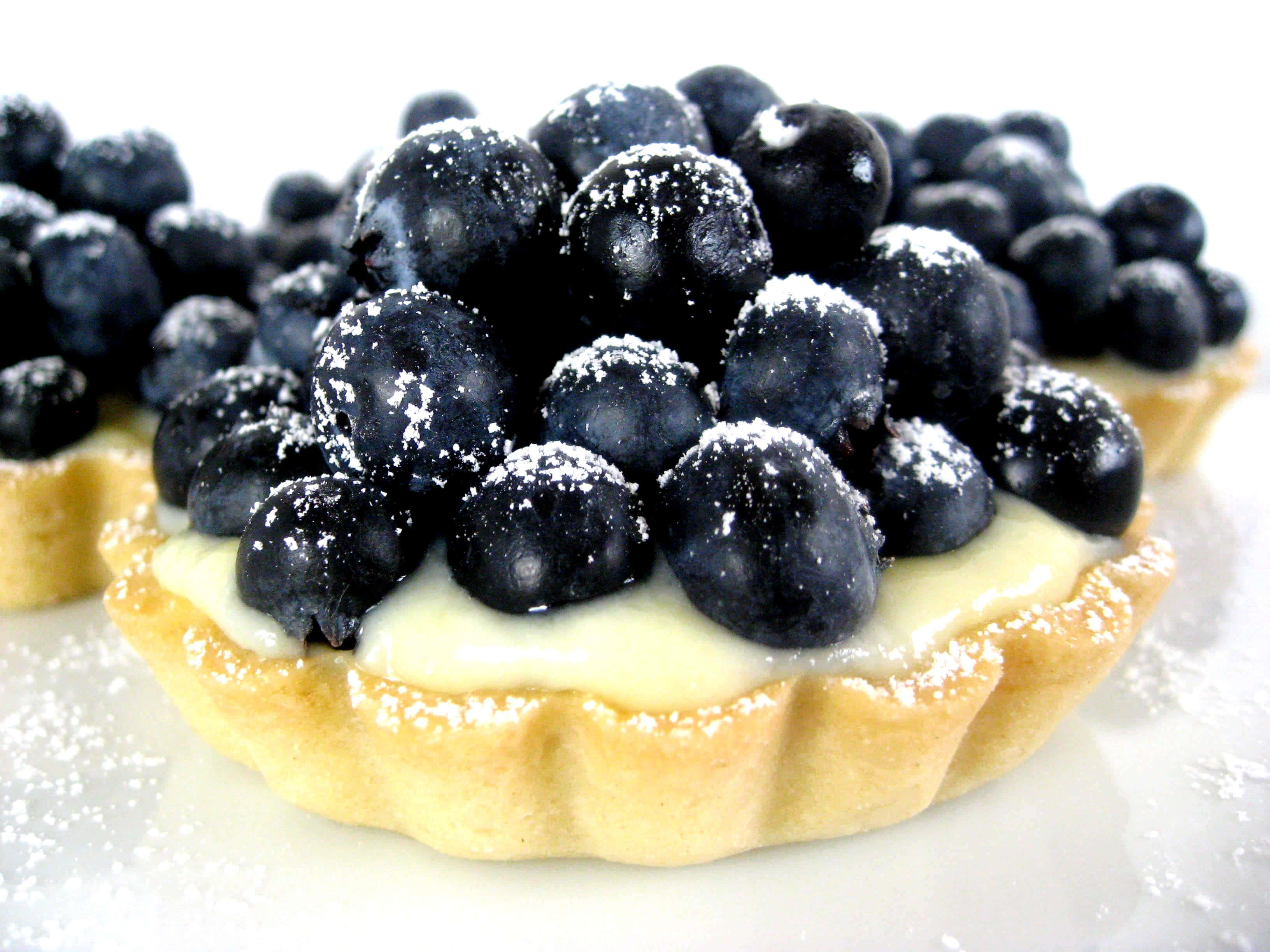 Blueberries Tart 桌布 壁紙 — 藍莓撻撒上糖粉，置於白色表面上的特寫。