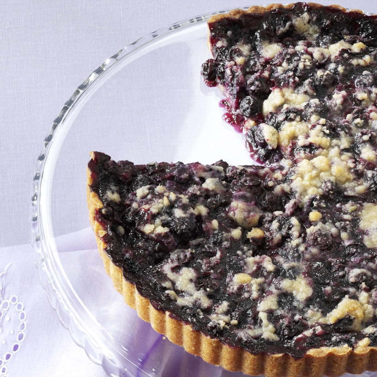 Blueberries Tart 桌布 壁紙 — 藍莓金寶撻近鏡，撻邊有坑紋，放在玻璃碟上，襯以淺紫色布。