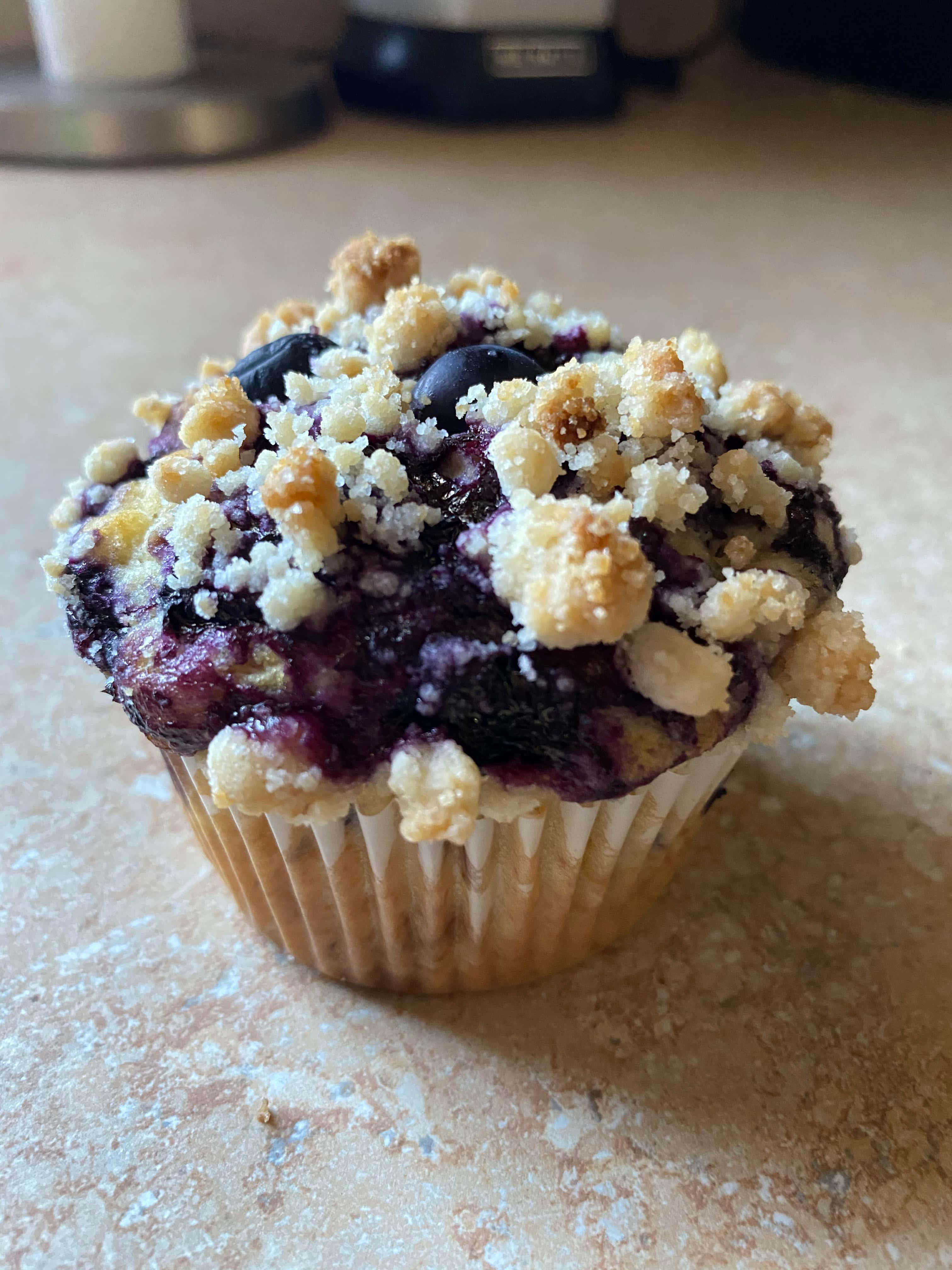 Blueberry Muffins 桌布 壁紙 — 藍莓鬆餅特寫，金黃酥粒頂層，置於灑滿麵粉的枱面上。