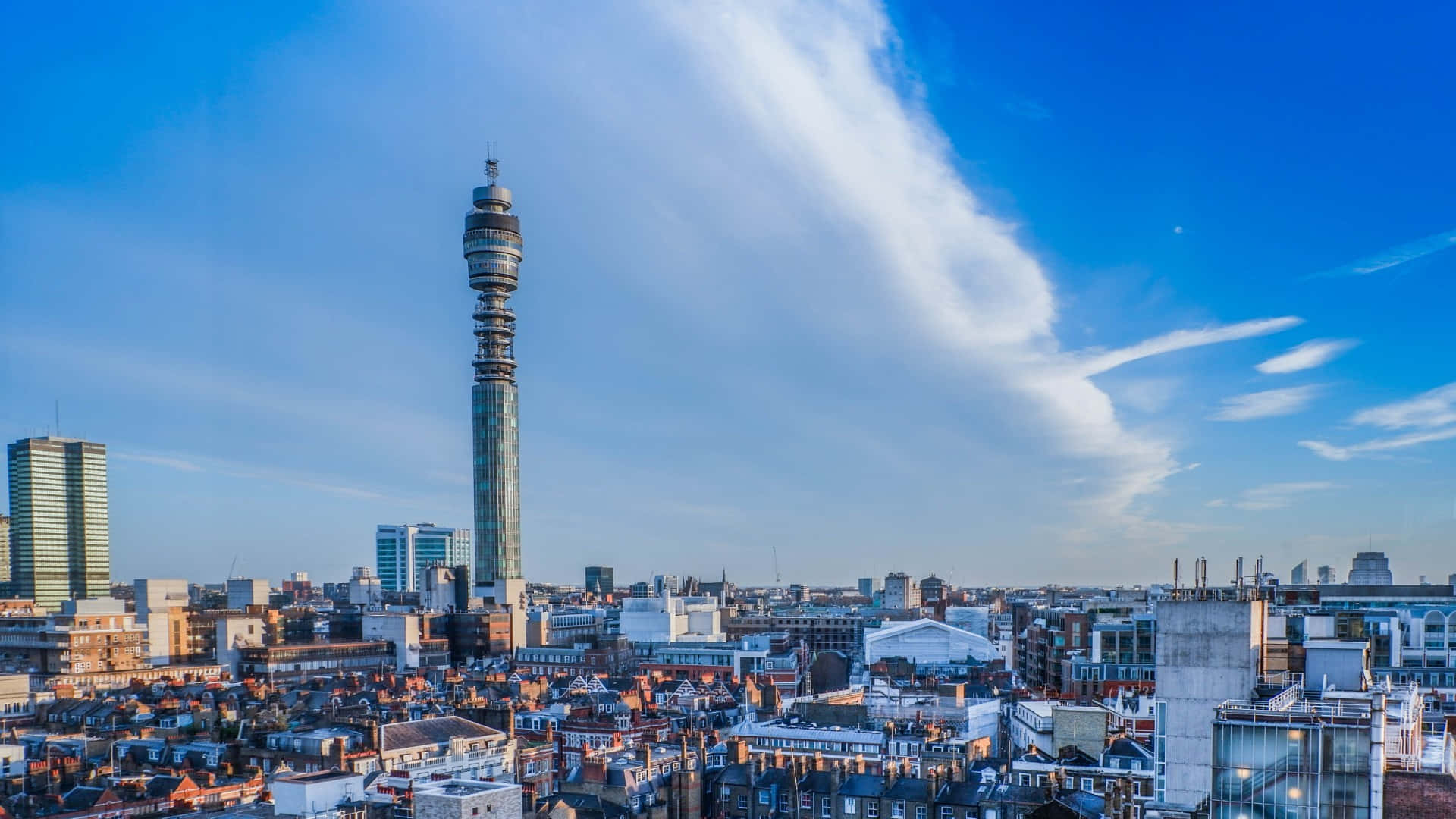 藍調倫敦BT塔桌面壁紙 壁紙 — 城市景觀的全景視圖，以一座高聳的電信塔為主，背景是明亮的藍天和薄雲。
