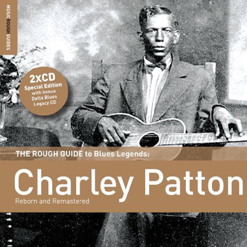 藍調傳奇人物查理·帕頓《粗獷指南》 壁紙 — Charley Patton 坐著拿著木結他的復古黑白肖像，帶有文字疊加，用於藍調音樂合輯。